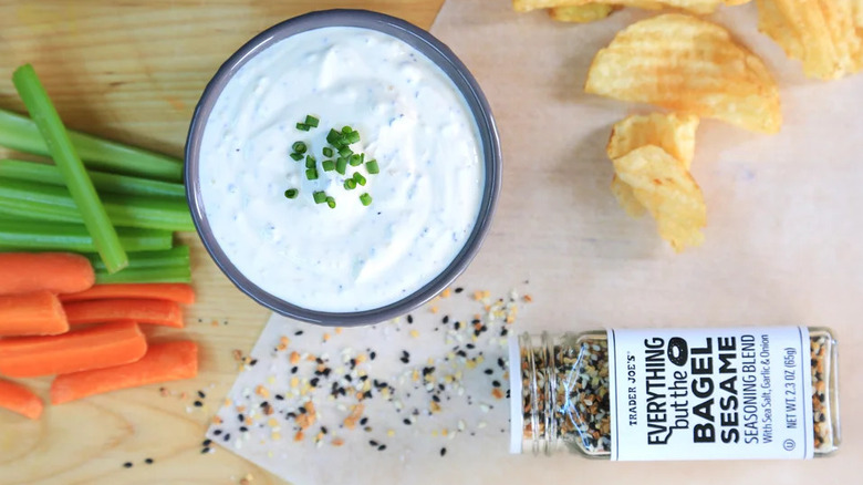 Jar of Trader Joe's Everything But The Bagel Sesame Seasoning Blend with a bowl of dip, raw veggies, and potato chips