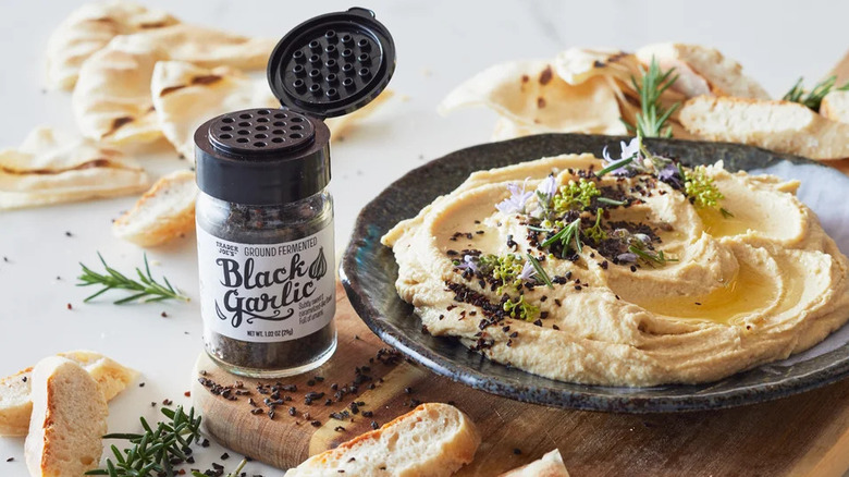 Jar of Trader Joe's Ground Fermented Black Garlic with a plate of seasoned hummus and bread