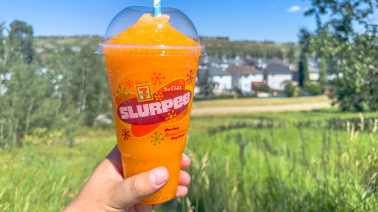 A hand holds up a 7-Eleven Slurpee outside