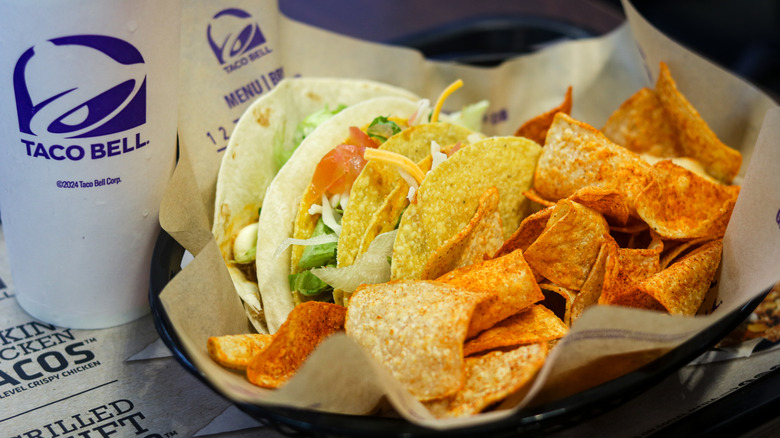 A basket of Taco bell tacos and seasoned chips with a soft drink.