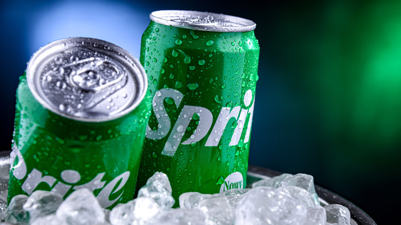 Two cans of Sprite beading with condensation sit in ice