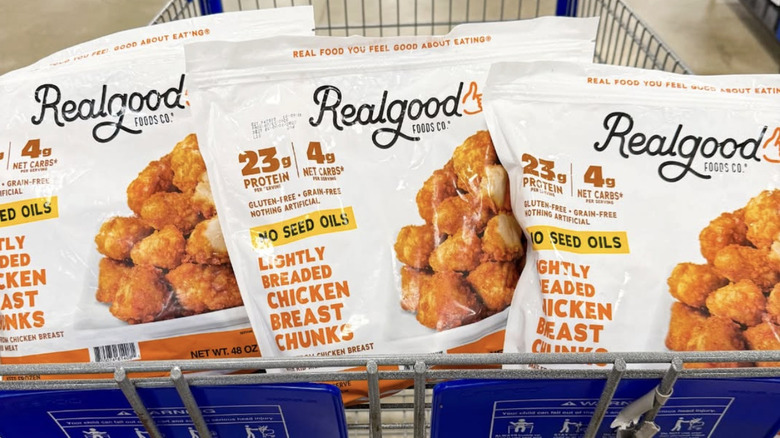 Three bags of Real Good Foods Lightly Breaded Chicken Breast Chunks in a shopping cart.