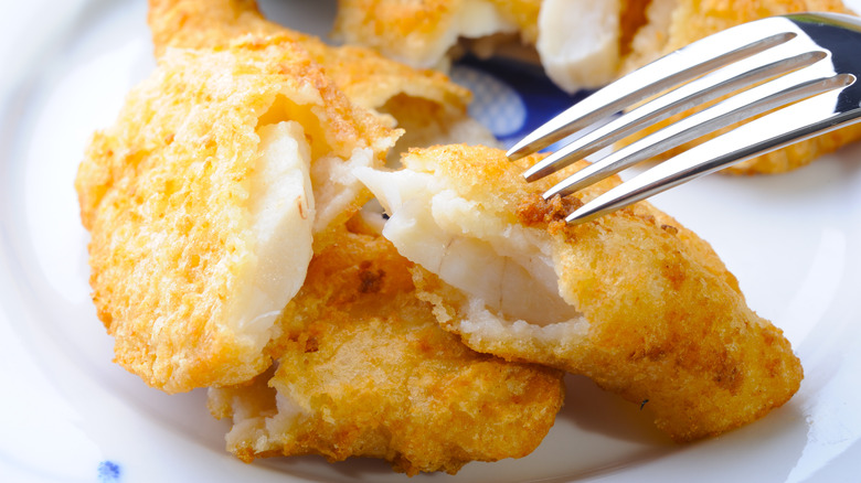 Fried cod fillets on a plate with a fork atop one of them.