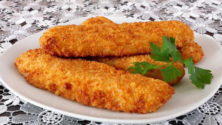 Breaded fish fillets sitting on a plate with a piece of cilantro.