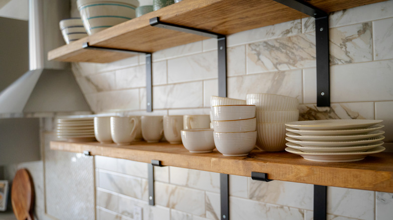 Open shelves in a kitchen displaying white and light-colored crockery