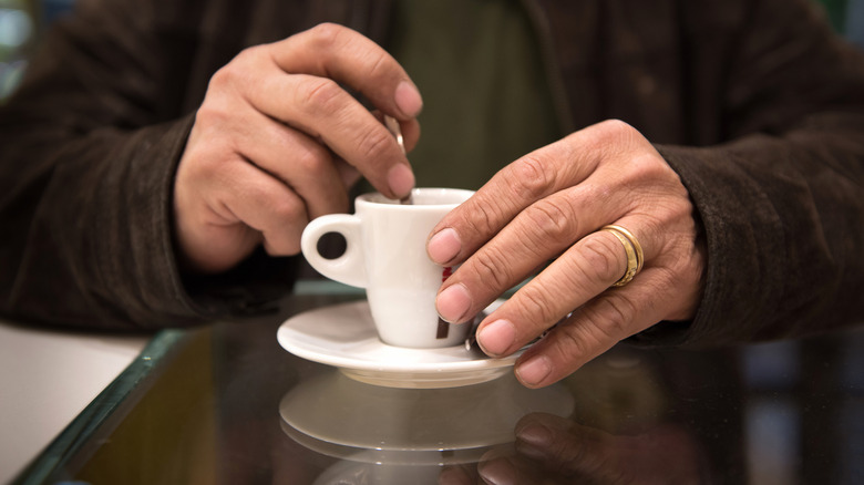 Closeup of an older person's hands stirring a small cup of coffee