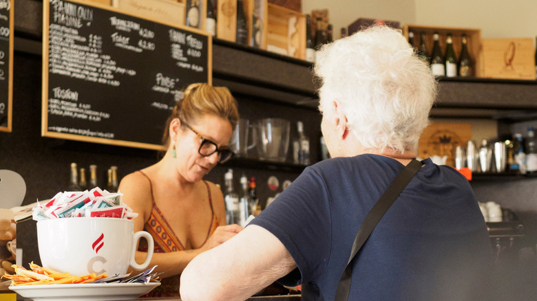 An elderly woman speaks with a barista