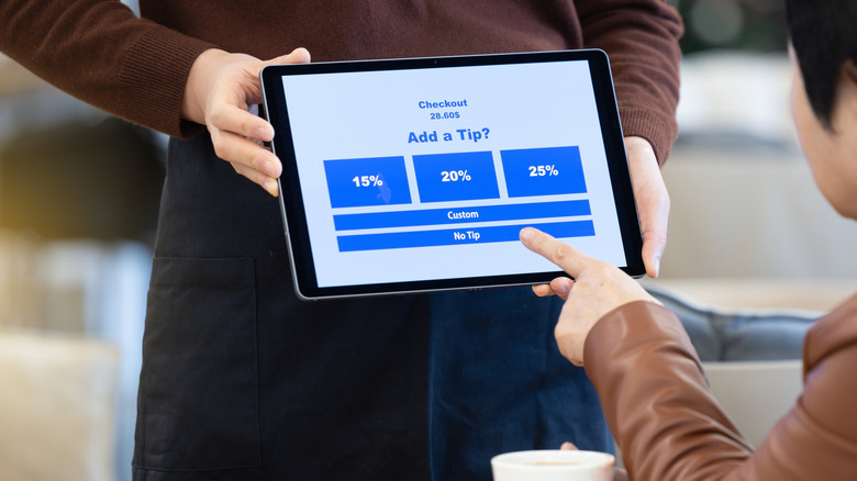 A server holds up a tip screen as an older person moves their index finger toward the No Tip option