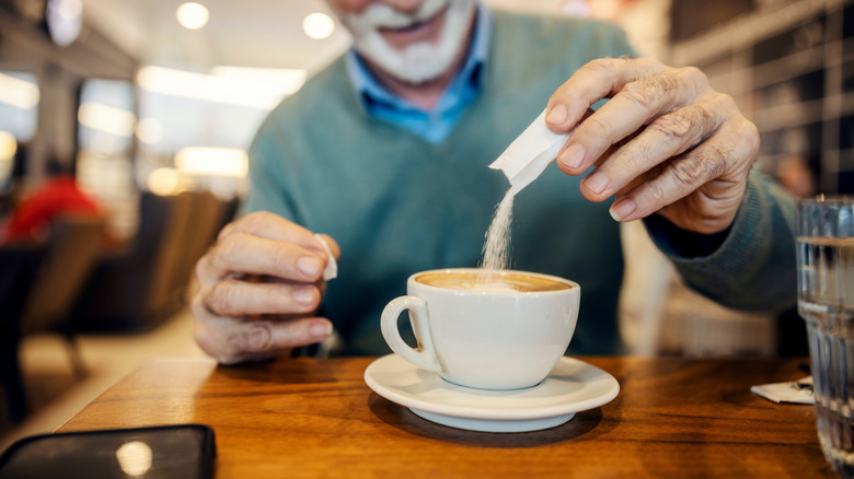 An older man pours sweetener into his coffee in a coffee shop