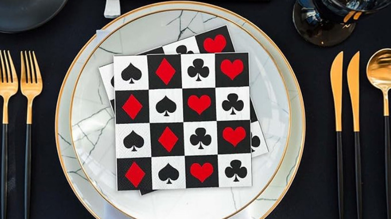 Napkins with card suits on a marbled plate, next to aesthetic gold and black cutlery