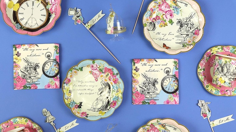 Napkin with flowers, a pocket watch, and the White Rabbit sit on a blue background next to Alice in Wonderland themed plates, cups, and party skewers