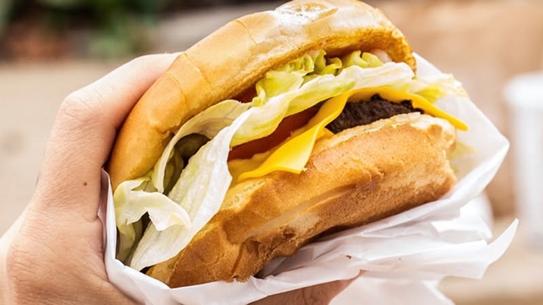 Hand holding a Jack in the Box burger wrapped in white paper