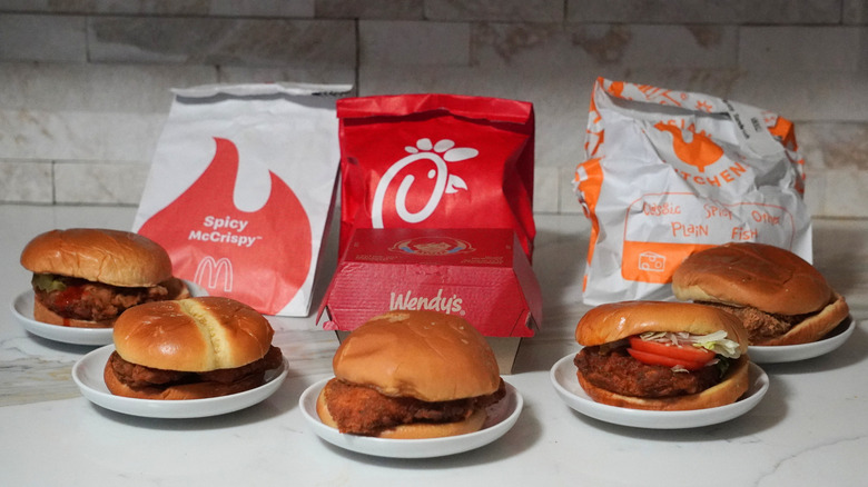 Five spicy chicken sandwiches in front of McDonald's, Chick-fil-A, and Popeyes bags.