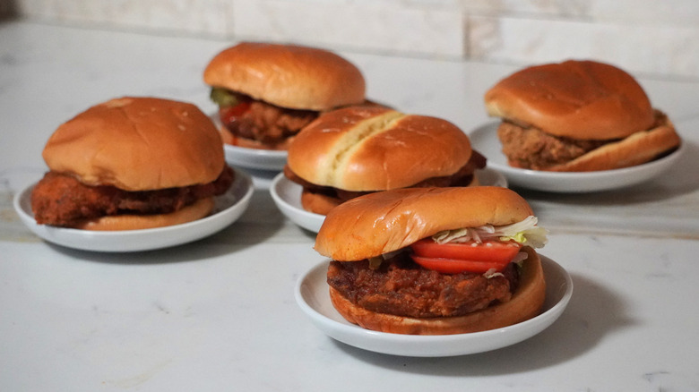 Five spicy chicken sandwiches on a marble countertop.