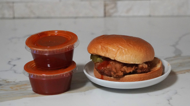WingStop Chicken Sandwich with Original Hot next to two plastic cups of Original Hot sauce.