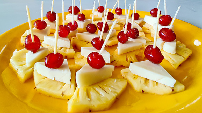 A plate of pineapple cheese skewers topped with cherries