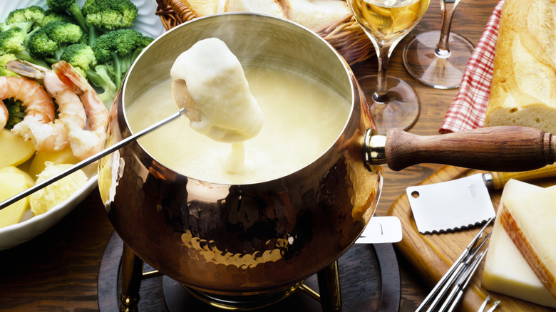 Someone dipping a fork into a cheese-filled fondue pot