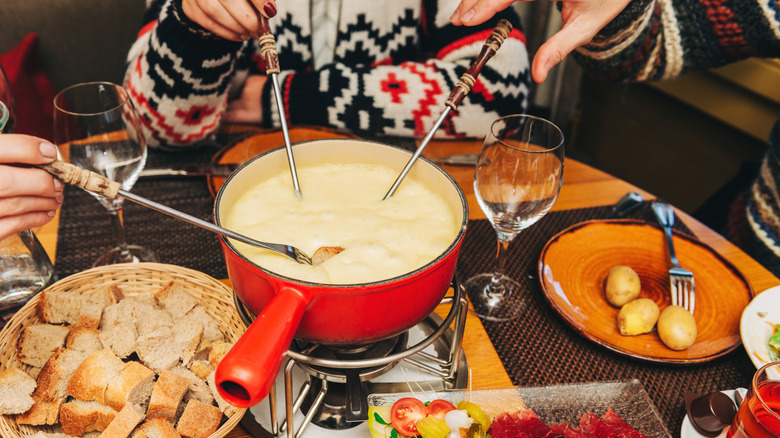 People dipping forks into a cheese-filled fondue pot
