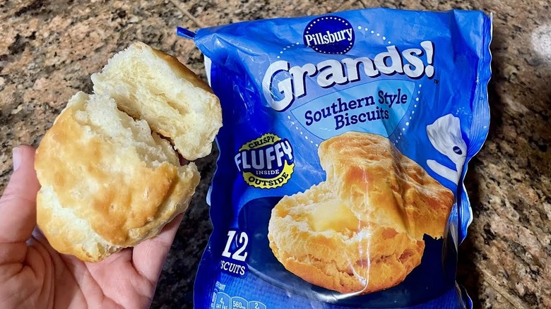 Hand holding Pillsbury Grands! Southern Style Biscuit over a bag of frozen ones