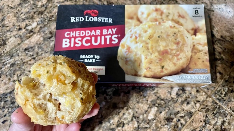 Hand holding Red Lobster Cheddar Bay Biscuit over box of frozen ones