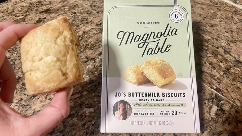 Hand holding Magnolia Table Jo's Buttermilk Biscuit over box of frozen ones