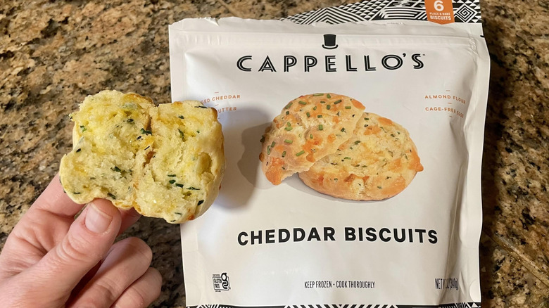 Hand holding Capello's Cheddar Biscuit over box of frozen ones