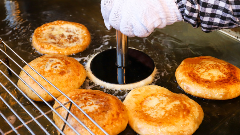 Hotteok being pressed on a griddle with oil