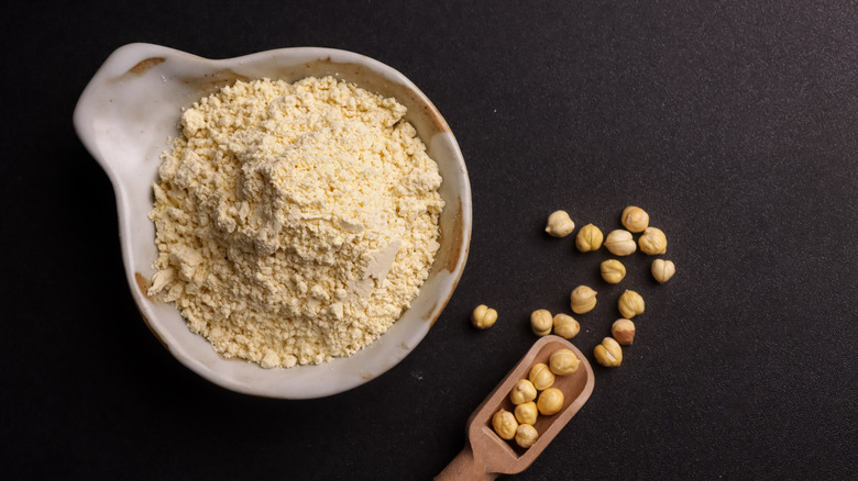 Chickpea flour in a bowl, some chickpeas and a wooden scoop on the side