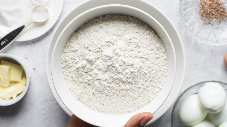 Bleached flour in a bowl with eggs and butter on the side
