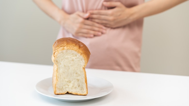 A young woman holds her stomach in pain in front of some bread