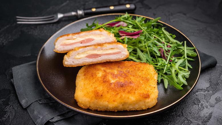 Chicken cordon bleu on a black plate with salad