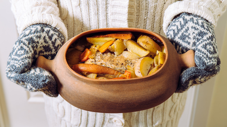 A person with knit oven gloves holding a pot of stew