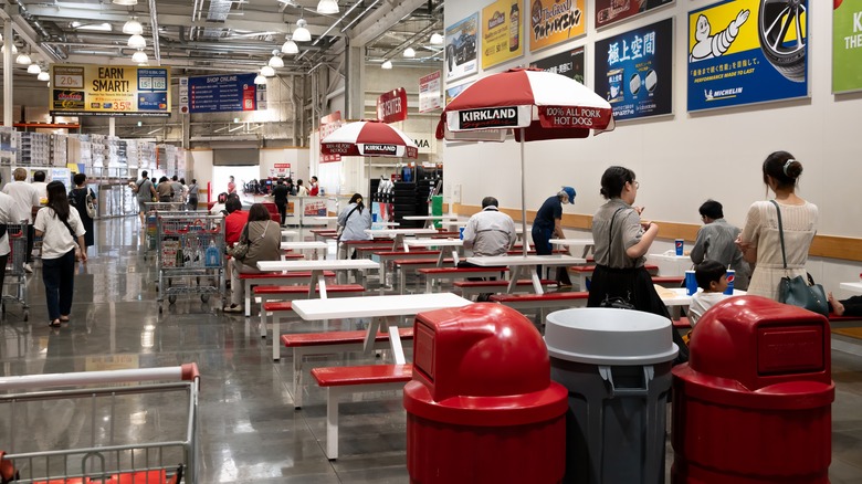Costco employee tidying up in a food court with customers scattered about