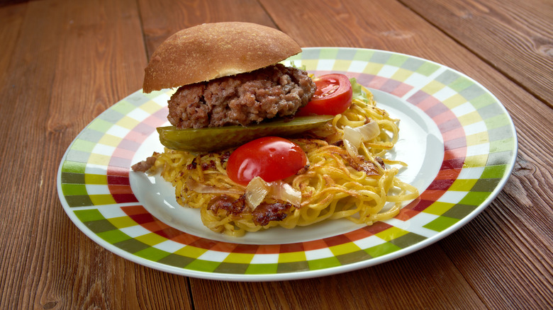 A chow mein sandwich served with a pickle and ground beef in a bun