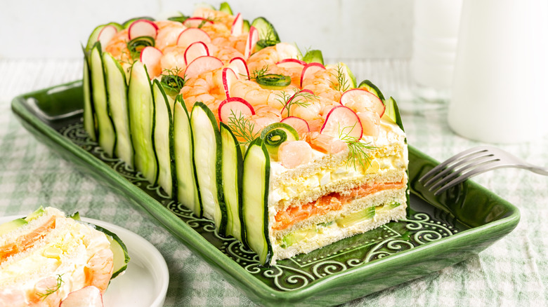 A frosted sandwich loaf with cucumbers for decoration and thinly sliced radishes on top