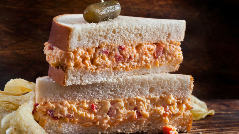 A pimento cheese sandwich stacked in two halves with a gherkin on top