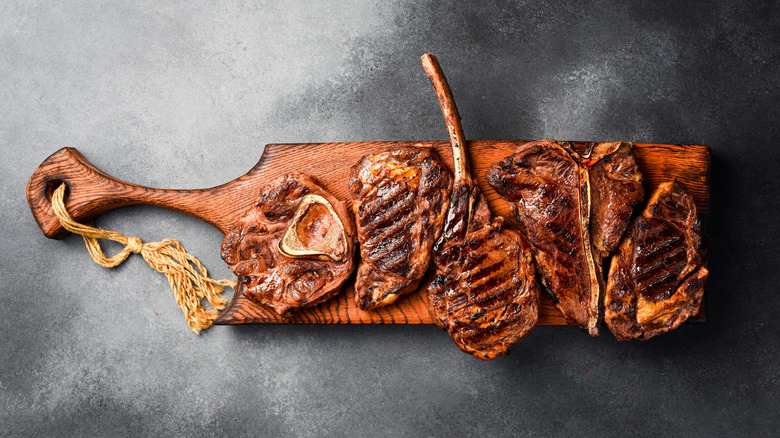 A variety of grilled steaks sitting on a wooden board