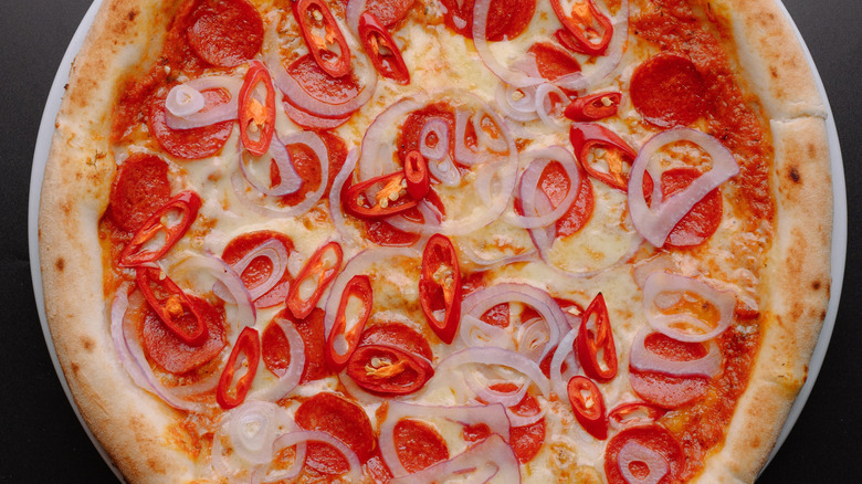A pizza topped with bright red spicy peppers and sliced onion