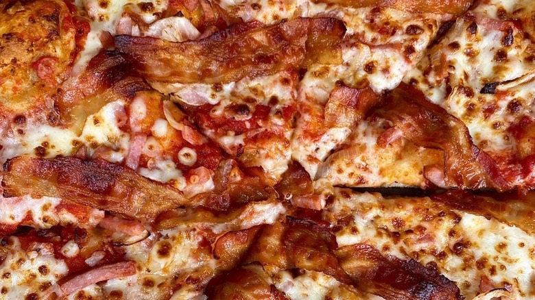 Strips of cooked bacon lie across a meat pizza