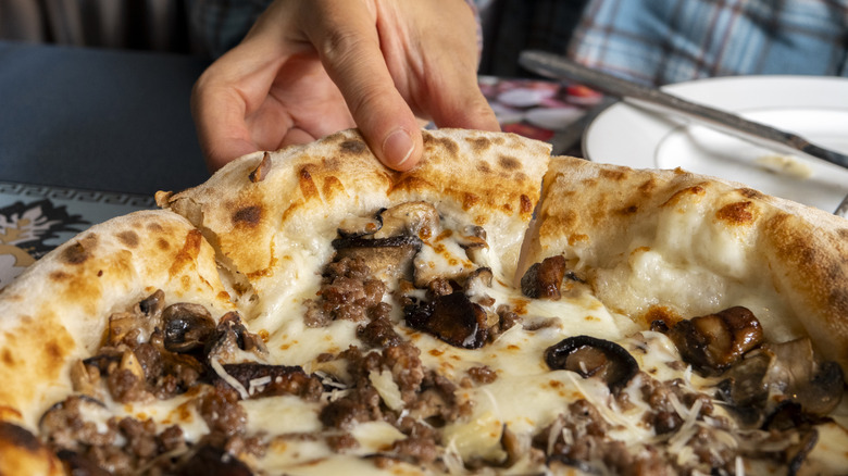 Hand grabbing a slice of freshly baked pizza with sauteed mushrooms