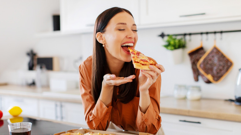 Someone enjoys a fresh slice of pizza at the kitchen counter