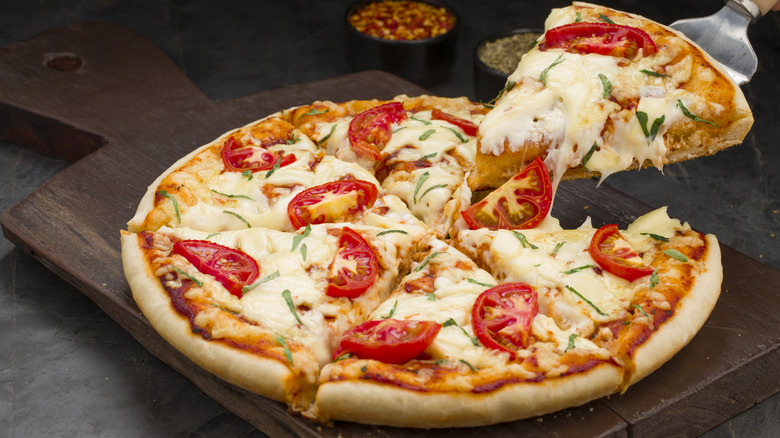 Pizza with fresh tomato slices and basil being served off of a wooden platter