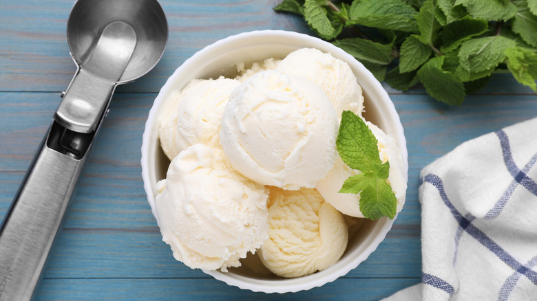 vanilla ice cream with mint and scoop on light blue wooden table, flat lay