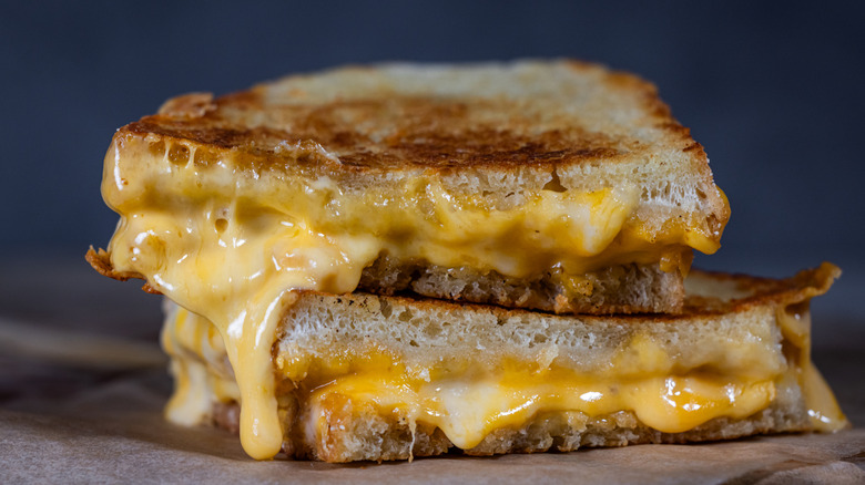 Grilled Cheese with melting cheese dripping from the inside. The sandwich is cut in half and placed on a wooden cutting board
