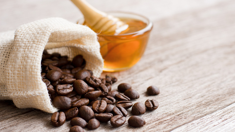 Coffee beans and honey in glass bowl isolated on white background.