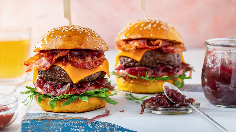 Two beef burgers with bacon, onion marmalade, tomato, cheddar cheese and arugula on a wooden board. Selective focus