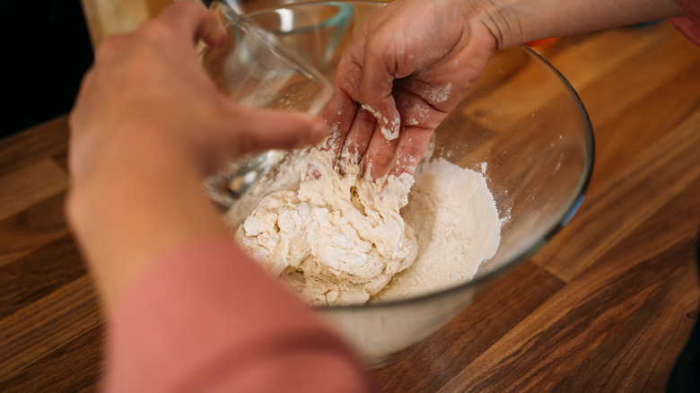 adding water to a bowl of dough while kneading