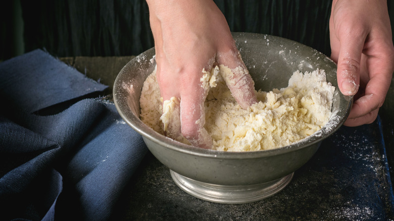 two hands making pastry dough in a metal bowl