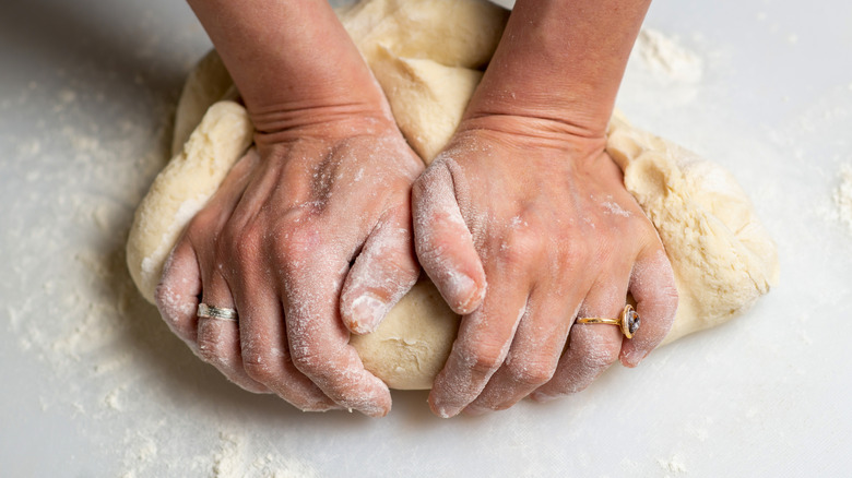 Two hands kneading dough on a floured white surface