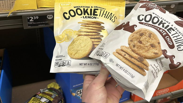 A hand holds out two bags of Benton's Cookie Thins